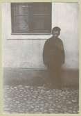 En man som står på kullersten vid ett fönster.