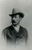 En bild på en man i hatt och mustasch.