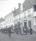 Häst och vagn på en gata i Kalmar samt en man som bär på ett par plankor i förgrunden.