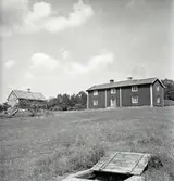 Vy med storstugan och källa i förgrunden.