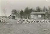 Stugbyn i Gårdby. Bostadshus och stenmur med grind.