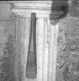 En inbyggd pelare med kapitäl och ett föremål.