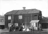 Grupp av människor framför en träbyggnad. Eventuellt i Gävle.