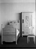 Säng och skåp av furu, stol av björk, vitlaserade med inlagda motiv av färgat trä. Delar av sängkammarmöbel ritad av Carl Westman 1901. Utställningen Svensk jugend. 