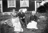 En man, två kvinnor och en flicka sitter i gräset vid sitt hus, Östhammar, Uppland