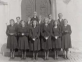 Kyrkoherde Gunnar Högberg i mitten med konfirmander utanför Hunnestads kyrka, Från vänster främre raden: Anne-Marie Pettersson, Elna Börjesson, Clauj Bartholdsson, Ulla Johansson, Maj Martinsson, Marian Bertilsson. Bakre raden: Göte Olsson, Sigvard Runevad, Bertil Johansson, Folke Irblad, Pauli Hallenberg.