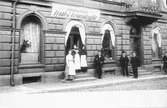 1883 köper Joseph Bauer huset vid Nygatan 16 i Jönköping. Personal står på trappan till Jönköpings Frukt-& Grönsaksaffär.