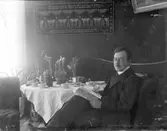 Läsande man vid dukat fikabord.