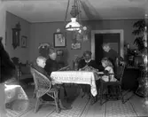 Två kvinno roch tre barn samlade runt ett bord i en salong.