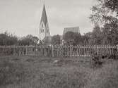 Garde kyrka på Gotland delvis dold bakom spjälstaket och träd.