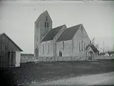 Hamra sandstenskyrka på Gotland med stigporten i öster. Till vänster i bild en byggnad utanför kyrkmuren (stall?).
