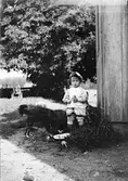 Liten pojke, sannolikt någon av Christiane och Ruben Liljefors söner, med hund ute på gården, sannolikt i Sverige