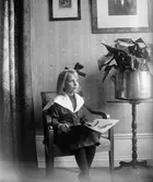 Ruben Liljefors dotter Marit sitter på stol och läser bok i hemmet, sannolikt i Sverige