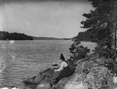 Kvinna, klädd i folkdräkt, sitter på klippa vid vatten, Dalarna