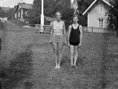 Ung man och kvinna i badkläder står utomhus, gårdsmiljöer, möjligen i skärgård, i bakgrunden, sannolikt i Sverige