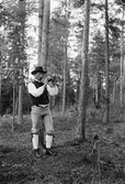 Man, klädd i folkdräkt, blåser vallhorn i skogen, sannolikt i Sverige