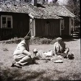 Kloar-Erik och Anders Lundgren sitter i gröngräset en stuga med sticktak/pärt, Dämmarehult, med kaffepanna på ett fotogenkök.
