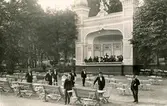 Musikpaviljongen vid sommarrestaurangen Tivoli med musikkår på estraden samt serveringspersonal vid parkmöblerna. Vykort.