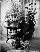 Man sitter på en stol vid ett bord, omgiven av blommor, Östhammar, Uppland