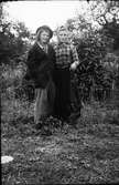 Två barn utklädda till gubbe och gumma i lummig trädgård. Flickan till höger är Lundgrens Ella.