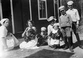 Christiane Liljefors med barnen Roland, Ingemar, Alf och Marit samt två andra kvinnor och hund utanför bostadshus, sannolikt i Sverige, omkring 1914