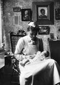 Kvinna med spädbarn i famnen i hemmet, sannolikt i Sverige