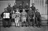 En grupp militärer, troligen under beredskapstiden, sittande på en trappa tillsammans med två kvinnor och en flicka. En med spelar på ett Granesso-dragspel, Männen är mycket solbrända med vita pannor efter mössorna.
