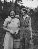 Två glada flickor i skogen med hinkar fulla av lingon. Lilly Larsson och Olas Märtha.