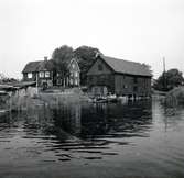 Kastmanska gården i Figeholm. I bilden syns ett bostadshus, en ekonomibyggnad, en brygga och två båtar.