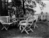 Drängen August Gabrielsson sitter i trädgården till Jonsjö säteri och spelar dragspel (klaver). Han omges i trädgårdsmöblerna av ungdomarna Jenny och Anna Lidberg, Evert Klasson och en hund. Sittplatsen är rundad och inhägnad med rabatt och staket med urnor på pelarna.