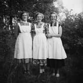 Personal vid ålderdomshemmet i Thårstorp poserar i trädgården - tre glada kvinnor i klänningar och vita förkläden.