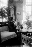 Rumsinteriör, en kvinna med ett litet barn i soffan.
Sigrid Thermaenius (född Grenander) med sonen Olle, född 1902-08-30.
Bilder från samma fototillfälle: OLM-92.149.128-1 och OLM-92.149.157-1