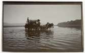Persien. En hästdragen vagn korsar ett vattendrag. Berg i bakgrunden.