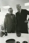 Kungligt besök på Gustavsbergs porslinsfabrik. Stig Lindberg förevisar stengodsskålar, sannolikt i Gustavsbergs Studio.
Personer: Kung Gustav VI Adolf och Stig Lindberg,