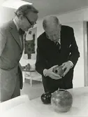 Interiör. Kungligt besök på Gustavsbergs Fabriker. Stig Lindberg och Kung Gustav VI Adolf. Förevisning av unikt stengods, sannolikt på Keramiskt Centrum.
Personer: Stig Lindberg och Kung Gustav VI Adolf