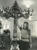 Interiörbild. Sannolikt Gustavsbergs Porslinsmuseum,1969. Marianne Landqvist, informationsansvarig på Gustavsbergs Fabriker förevisar en stående kandelaber gjord 1870.
Personer: Marianne Landqvist.