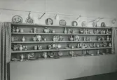 Interiörbild. Utställning med föremål från Gustavsbergs fabriker. Fat och vaser. Fajanser målade i rödlera, polykrom dekor. Konstnärer: Wilhelm Kåge och Stig Lindberg. 1942. Plats okänd.