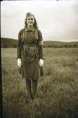 Anna-Lisa i Hugalyckan står uniformsklädd ute på ett stort gräsfält. Hon har en mössa försedd med ett märke med vitt kors och vita handskar, samt armbindel.