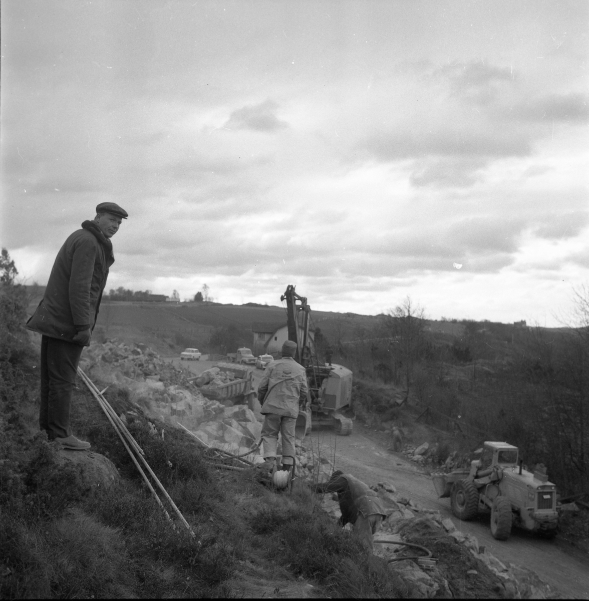 Percy Heldebrandt, Excavator and other road machinery in work at Galgen in connection with the motorway construction at Gränna/Röttle, stage II. An unknown man stands at a height to his left and looks at the photographer. At the house stands a police car - Volvo Amazon.