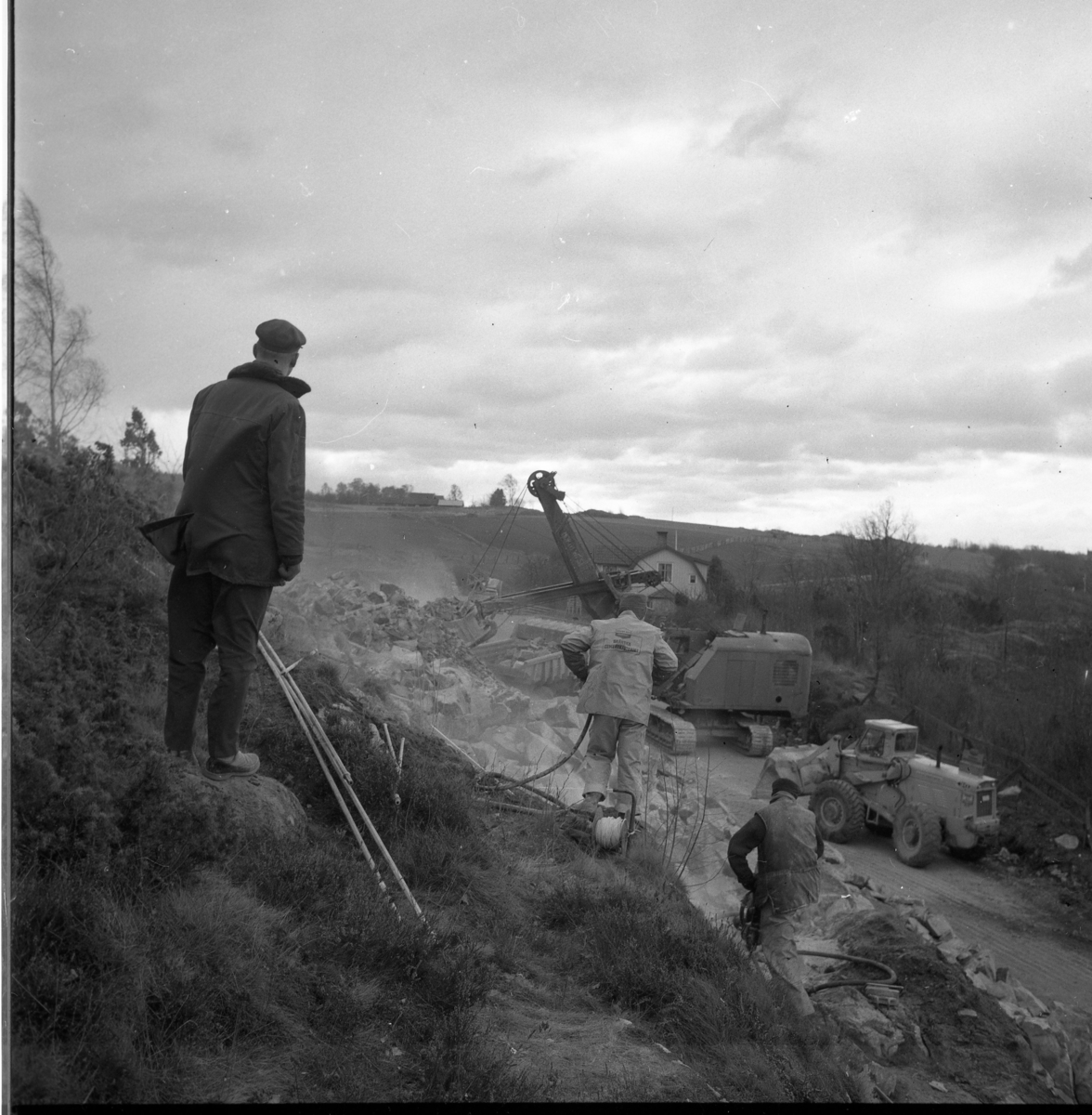 Percy Heldebrandt, Excavator and other road machinery in work at Galgen in connection with the motorway construction at Gränna/Röttle, stage II. An unknown man stands at a height to the left and looks towards the workplace. At the house stands a police car - Volvo Amazon.