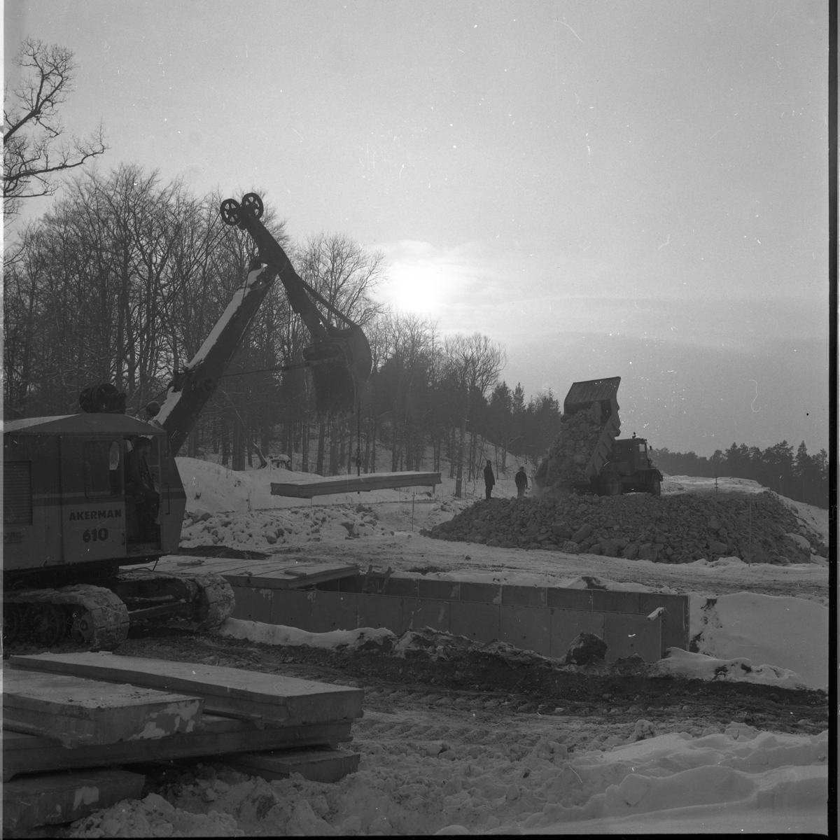 Percy Heldebrandt, Grävskopa och lastbil i arbete i samband med motorvägsbygget vid Gränna/Röttle, etapp II. Lite snö på marken.