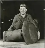 Personvagnsreparatör Einar Larsson, vid Trafikaktiebolaget Grängesberg–Oxelösunds Järnvägars järnvägsverkstad i Eskilstuna, visar upp bufferten som föll ner på hans fot i samband med en arbetsplatsolycka. Tack vare skyddskorna han bar så klarade han sig utan allvarliga skador.