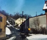 Samuel Norbergsgatan – Friareliden, okänt årtal. En backe svänger åt höger utefter Störtfjället. Fabriksbyggnad ses till vänster och garage samt villor till höger. Elledningar passerar över byggnaderna och det är snö och halka på marken.