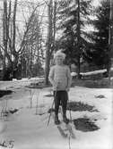 En pojke står på ett par skidor i en skog, troligtvis 1920-30-tal. På marken ligger snö. Det är samma gosse som 2018_0100.