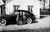 Tre pojkar står vid en Volvo PV, parkerad invid en husgavel. Pojken i mitten är på besök hos bröderna Tommy och Kennet Svensson, som är likadant klädda.