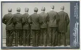 Ateljéporträtt - Sju män iklädda kostym, porträtterade bakifrån. Männen är: Harald Falk, David Nylund, Elias Stenius, Yelverton Tegner, Manne Ekman, Albert Falk samt en oidentifierad man, Uppsala 1902