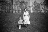 Vårdarinnan Karin Hasselberg håller ett litet barn i handen.
De står framför skolhemmet Stretered. Ca1940-tal.