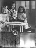 Reprofotografi av bild på tre barn med en uppslagen bok. I fotografens egna anteckningar står det 