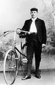 Man med knickers och mössa står bredvid en cykel i en fotostudio.