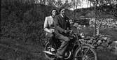 Syskonen Ivar och Margit sitter på en motorcykel om våren vid en husruin. De har varsin pingstlilja; Ivar har fäst sin på kavajslaget och Margit håller sin i handen.